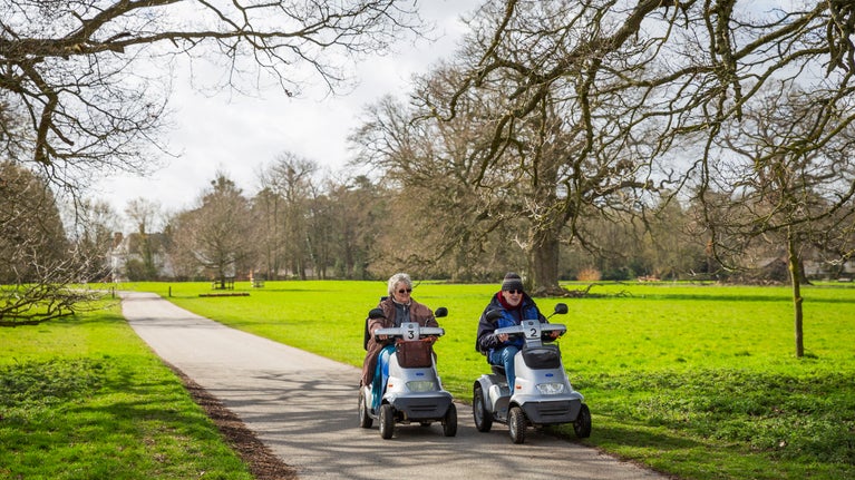 Two people in mobile trampers exploring along a level path through winter parkland
